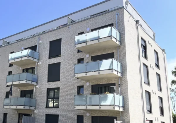 Ein hellgraues Mehrfamilienhaus mit sechs Balkonen vor einem hellbauen Himmel.